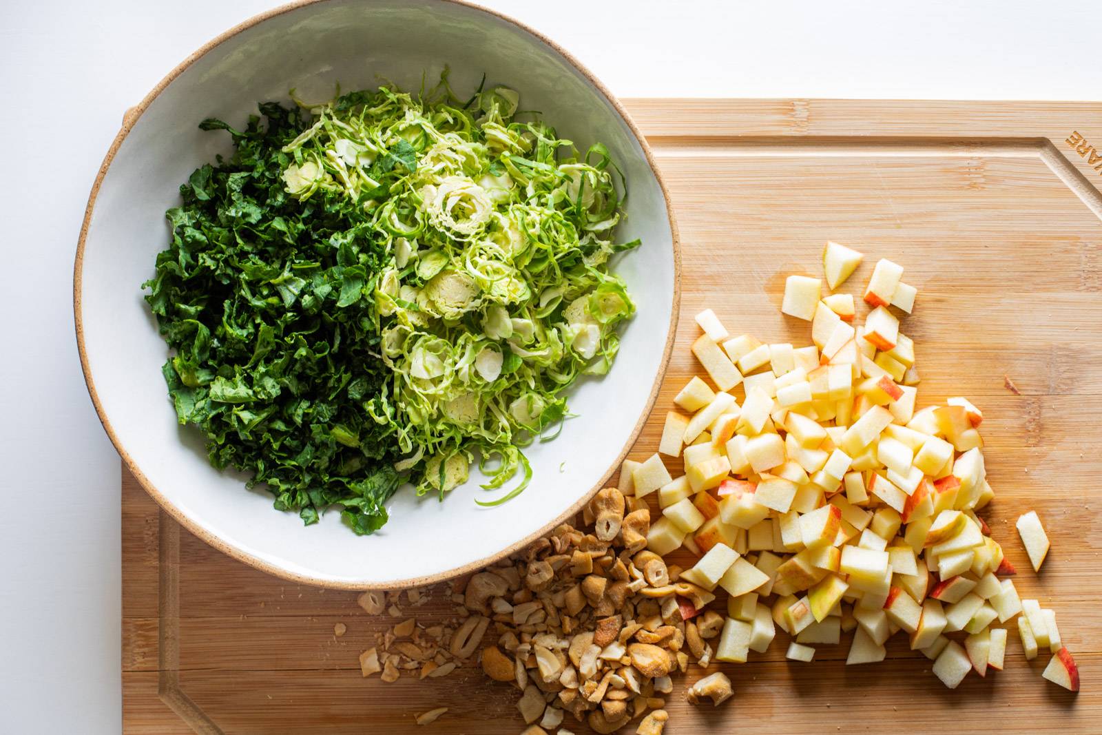 Kale和Blussel Sprouts在一个碗里切碎,苹果和腰果在切板上切片